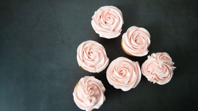 Bloemen spuitmondjes: cupcakes met gespoten roze botercrème rozen op een donkere ondergrond