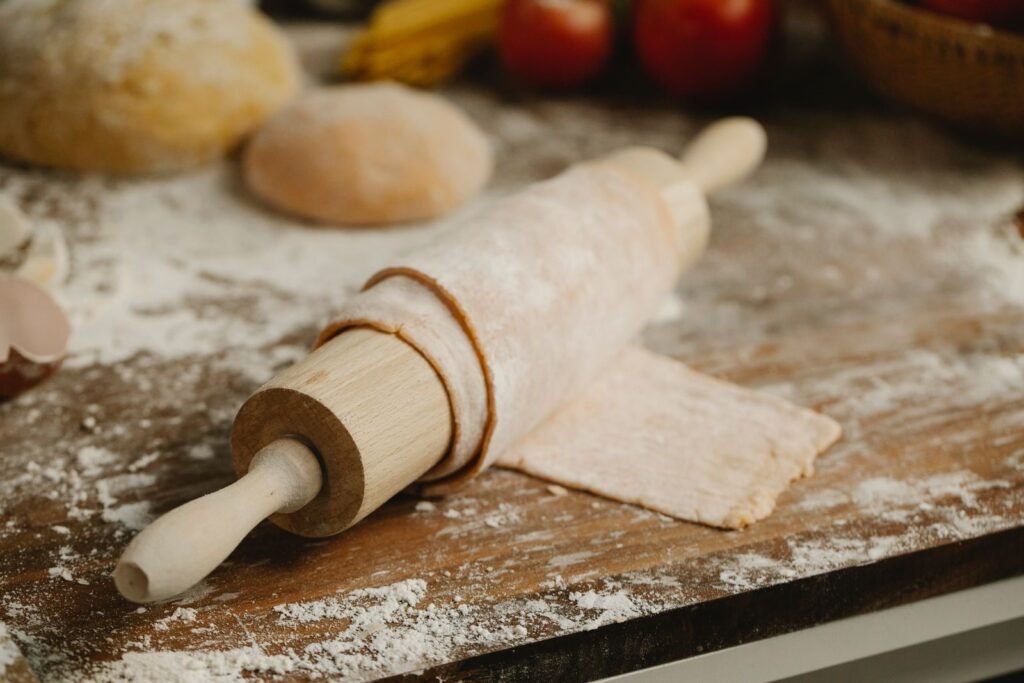 Deegroller met afstandhouders: houten deegroller op uitgerold deeg met bloem en deegbollen