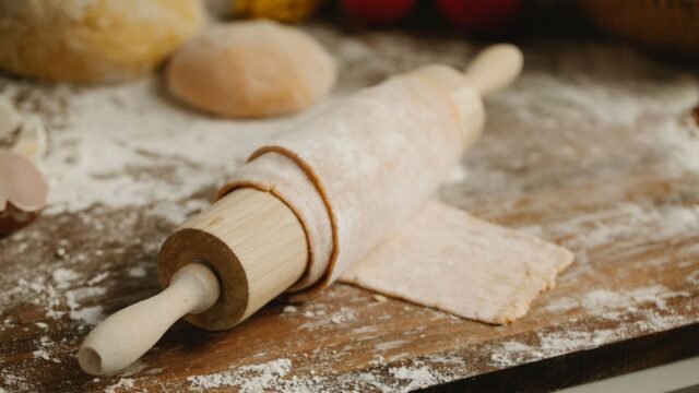 Deegroller met afstandhouders: houten deegroller op uitgerold deeg met bloem en deegbollen