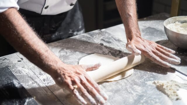 Deegroller rvs: bakker rolt deeg uit op een met bloem bestoven werkblad