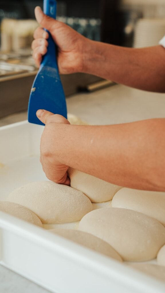 Deegschraper flexibel kunststof: bakker verdeelt deegbollen met een blauwe kunststof schraper in een bak