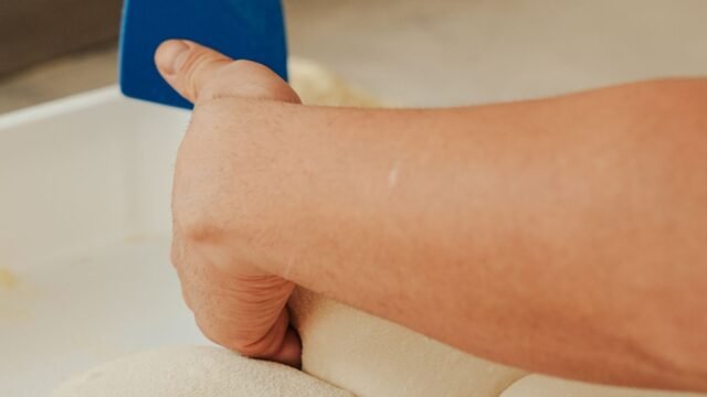 Deegschraper flexibel kunststof: bakker verdeelt deegbollen met een blauwe kunststof schraper in een bak