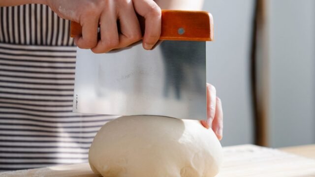 Deegschraper rvs: brooddeeg wordt verdeeld met een metalen deegschraper op een houten plank