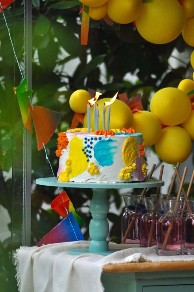 Eetbare foto taart: kleurrijke verjaardagstaart met kaarsjes op een taartplateau tussen ballonnen
