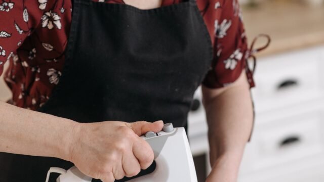 Handmixer bakken: vrouw mengt beslag met een witte handmixer in een rvs kom