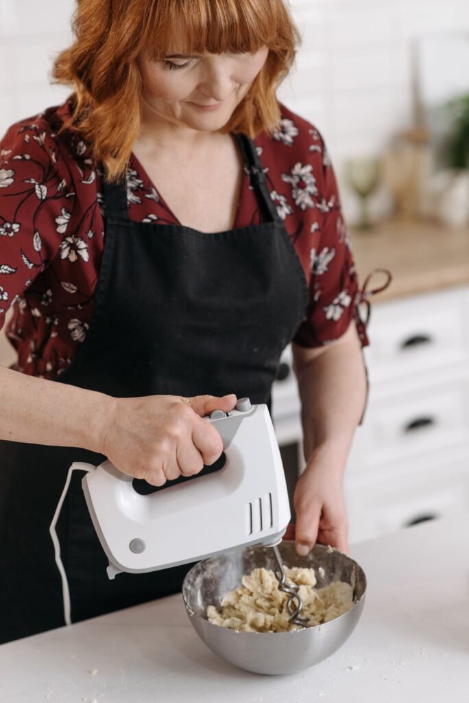 Handmixer bakken: vrouw mengt beslag met een witte handmixer in een rvs kom
