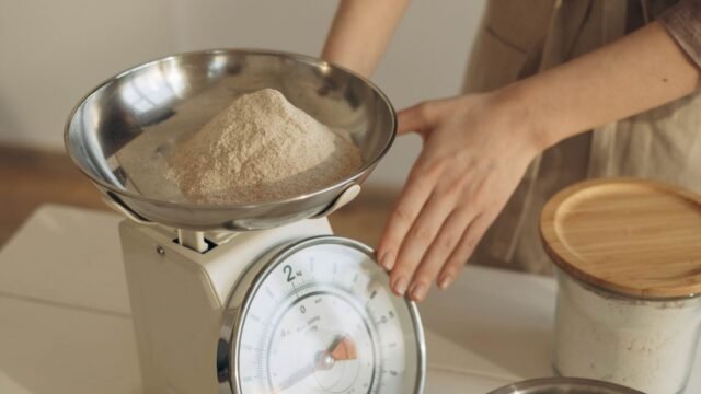Keukenweegschaal met kom: vrouw weegt bloem af in de metalen kom van een analoge weegschaal
