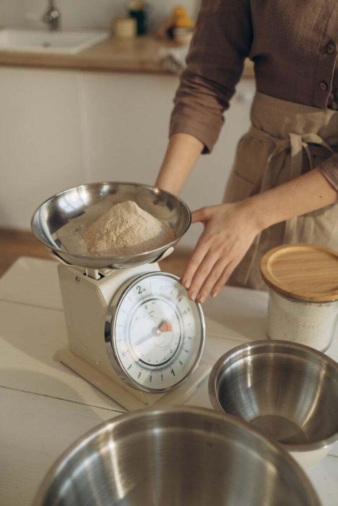 Keukenweegschaal met kom: vrouw weegt bloem af in de metalen kom van een analoge weegschaal