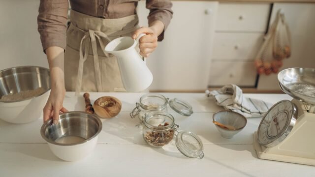 Keukenweegschaal tot 10 kg: vrouw giet melk in een kom tussen bakingrediënten met een weegschaal ernaast