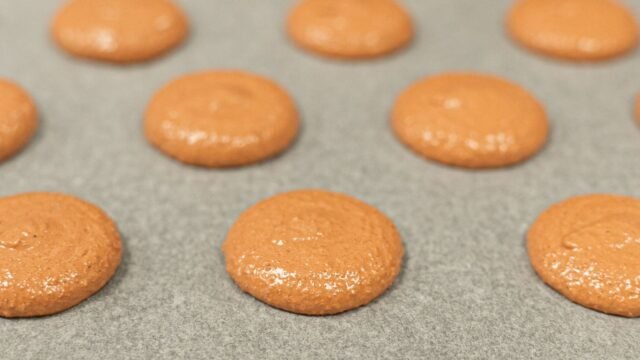 Siliconen bakmat macarons: oranje macaronschelpen gespoten op een bakmat