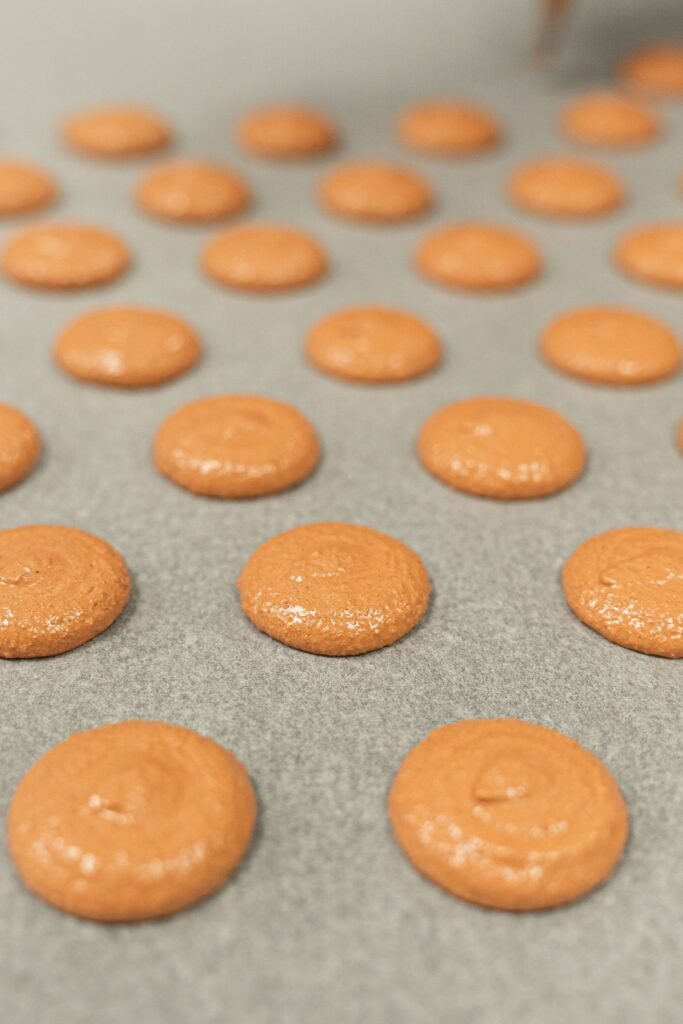 Siliconen bakmat macarons: oranje macaronschelpen gespoten op een bakmat