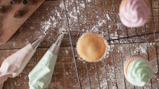 Spuitmondje ster 1M: cupcakes met gespoten rozetten en spuitzakken op een afkoelrooster