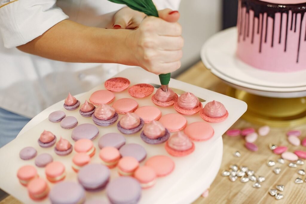 Spuitzakken Blokker: banketbakster spuit macarons met een groene spuitzak naast een roze taart