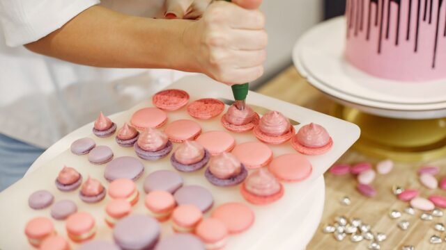 Spuitzakken Blokker: banketbakster spuit macarons met een groene spuitzak naast een roze taart
