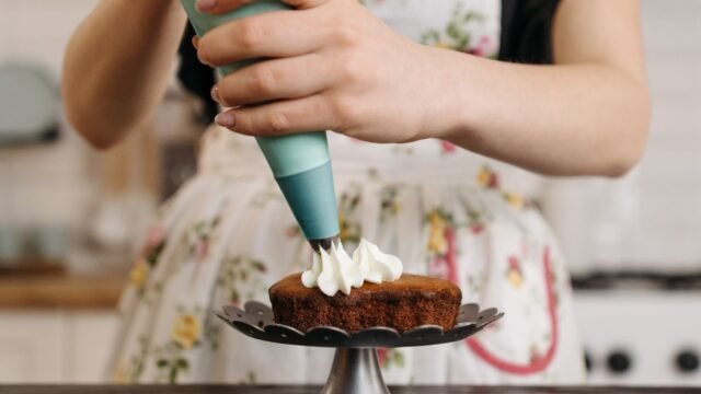 Spuitzakken gebruiken: vrouw spuit botercrème met een spuitzak op een taartje