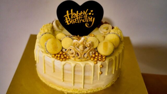 Suikerparels goud: verjaardagstaart met gouden parels, macarons en een zwarte Happy Birthday-topper