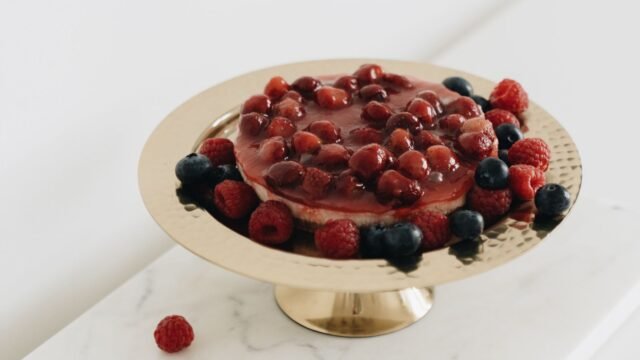 Taartplateau goud: cheesecake met rode bessen op een gouden taartplateau op voet