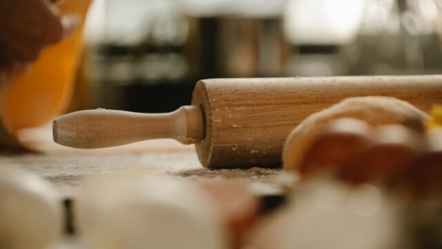 Verstelbare deegroller hout: houten deegroller op een met bloem bestoven tafel naast deeg