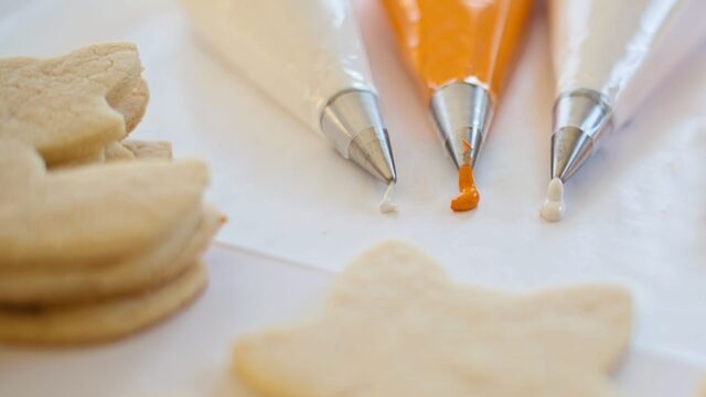 Wegwerp spuitzakken rol: drie gevulde wegwerpspuitzakken met glazuur naast uitgestoken koekjes